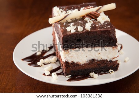 Chocolate mousse cake with white creamy layer on a white plate, on a wooden table, garnished with white chocolate.