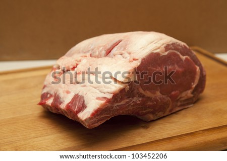 Raw prime rib beef roast, bone-in, seven pounds, on a wooden cutting board.