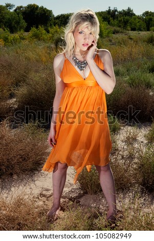 Dramatic full length outdoor portrait of beautiful blonde woman standing in the middle of the desert, touching her face