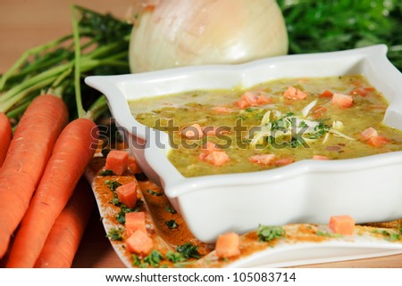 Carrot Soup surrounded by carrots with green tops, and an onion; dish is covered with a light curry coating.