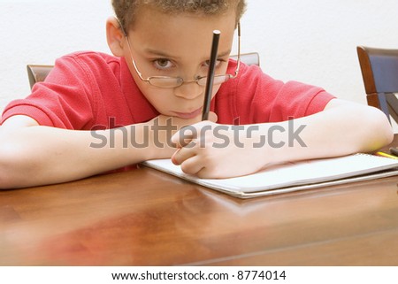 Left handed young boy wearing glasses reluctant to do homework not paying attention, staring into space.