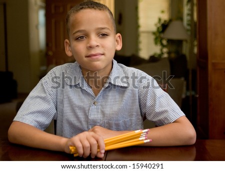 young boy at table holding pencils, ready for school to get started