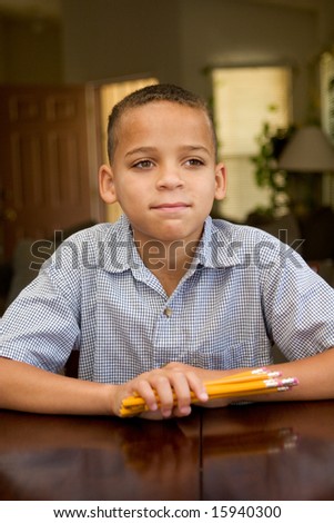 Young boy holding pencils, sitting at table ready for school.