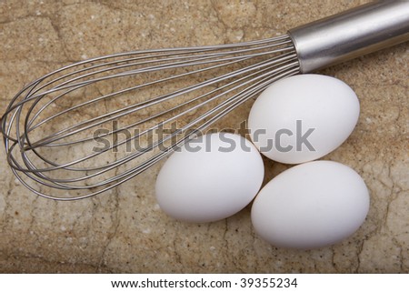 Close up view of three eggs and wire whisk