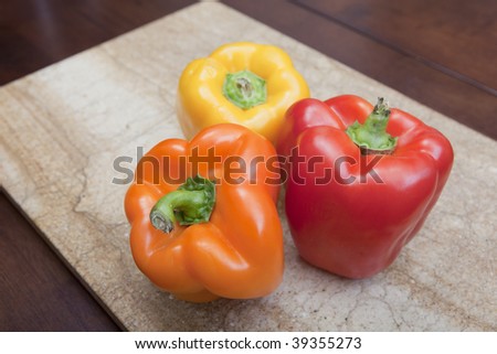 Three bell peppers on cutting board in red, yellow and orange.