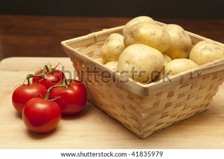 Basket of fresh raw potatoes next to red ripe tomatoes on the vine
