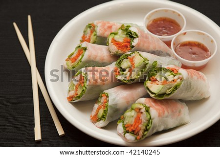 Horizontal view of shrimp spring rolls with sweet chili sauce, next to chopsticks.