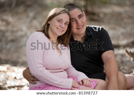 Portrait of a young, happily married couple outdoors in a park, smiling at the camera.