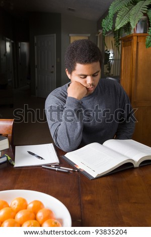 Hard working African American teenaged student, studying at home with stack of books and study materials.
