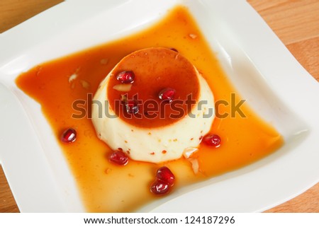 Single serving of creme caramel or flan dessert topped with syrup and pomegranate seeds.