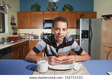 Handsome mixed ethnicity teenaged boy sitting in kitchen ready to eat a peanut butter and jelly sandwich.