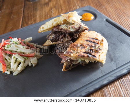 Gourmet medium-rare steak and Gorgonzola cheese grilled panini served with a red and green cabbage coleslaw on a cast iron plate with a honey mustard.