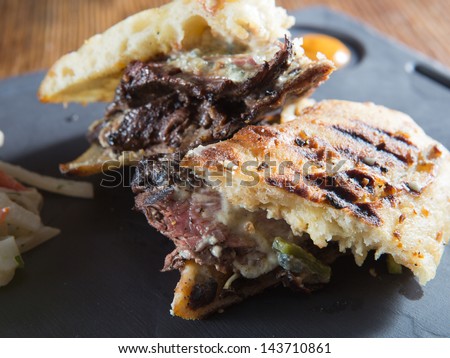 Gourmet medium-rare steak and Gorgonzola cheese grilled panini served with a red and green cabbage coleslaw on a cast iron plate with a honey mustard.