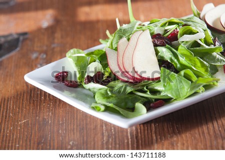 Rustically styled single serving of gourmet raw crispy spinach salad with dried cranberries and sliced red pears.