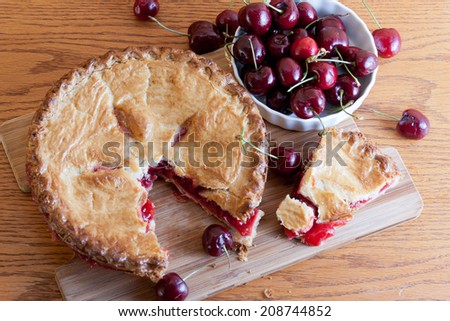 Slice of hot cherry pie removed from the whole garnished with red ripe cherries.