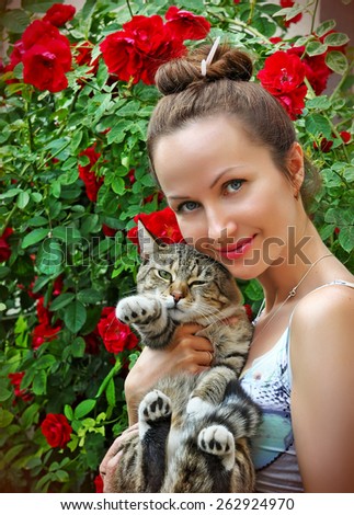 beautiful young woman with tabby cat in the garden with blooming roses
