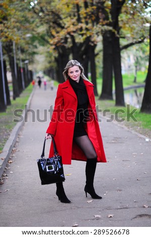 young beautiful woman standing at the mall road in a red coat at the autumn park