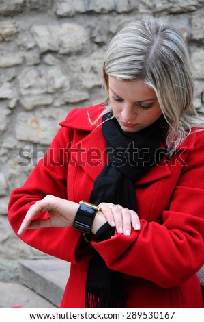 young beautiful woman looks at the clock in a red coat at the autumn park