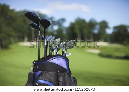 Golf bag and clubs in front of de focused green with sand traps
