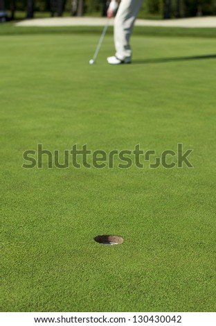 A golfer lines up a putt on a green. Focus on the hole.