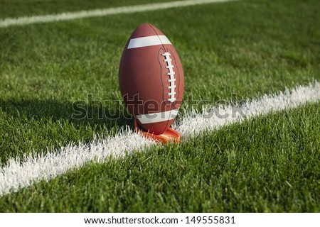 A college football sits on a tee at a yard line ready for kickoff