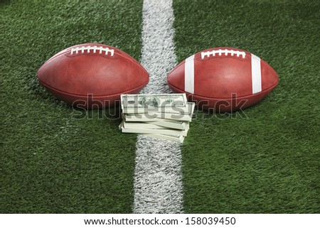 Pro and college style footballs with a pile of money on the line