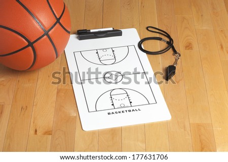 A basketball with coach\'s clipboard and whistle on a wooden gymnasium floor