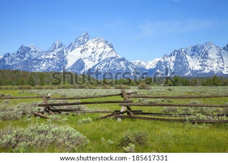 A rail ranch fence crosses a field below the Grand Teton mountains in Wyoming