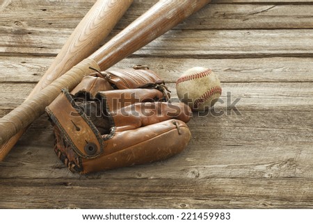 An old baseball, mitt and wooden bats on a rough wood surface