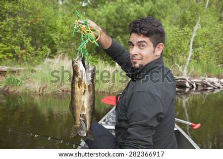 A handsome young Hispanic fisherman in a canoe holds up a stringer of walleyes on a Minnesota lake