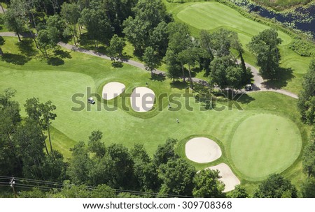 Aerial view of a golf course fairway and green with sand traps, trees and golfers