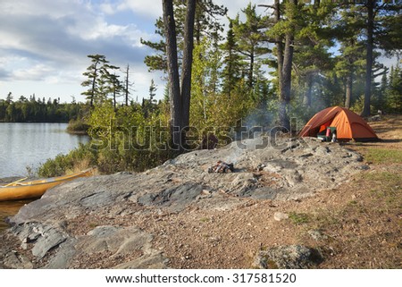 Campsite with orange tent and canoe on a lake in the Boundary Waters Canoe Area Wilderness of Minnesota