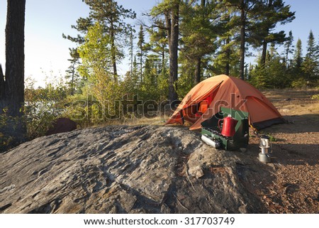 A campsite with an orange tent and cook stove in the north woods of Minnesota
