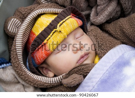A newborn baby sleeps warmly dressed in a wheelchair in the street