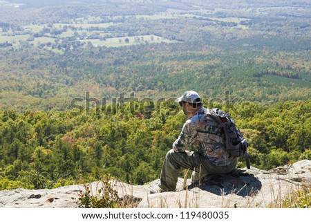 A man sits on the edge of a cliff and looking to the valley landscape