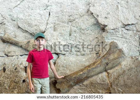 A boy stands near the wall where the fossilized dinosaur bones (Dinosaur National Monument, Utah)