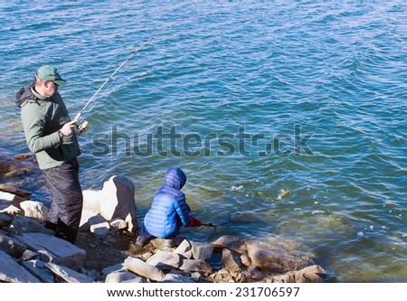 Father and son catch trout in the lake. Adult fish caught and gets it in the net, which keeps the child