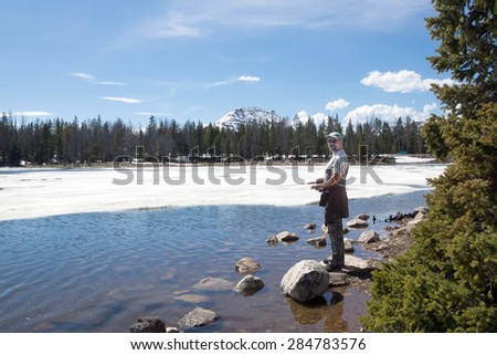 Fisherman catches a fish in a thawed patch of ice on Lost Lake.   Uinta-Wasatch-Cache National Forest, Utah