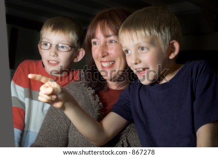 Family viewing a computer screen, with one child pointing.  Focus on Woman and far child\'s faces.