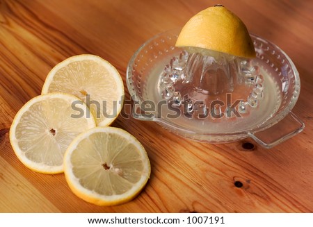three slices of lemon with lemon juice and squeezed half of lemon on wooden table, dappled light.  Fairly shallow dof; focus on squeezer and far lemon slice.