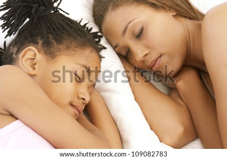 African American mother and her cute daughter with spiky hair sleeping side by side on white pillows.