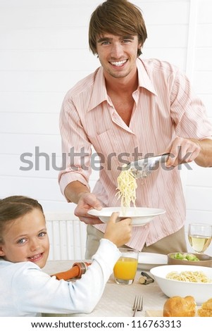 Happy young father serving spaghetti to his his small son while seated at the dinner table