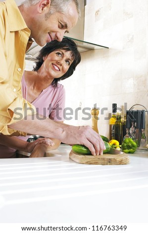 Husband slicing a cucumber on the kitchen counter watched by his adoring wife