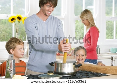 Young family cooking spaghetti with Dad placing the pasta in a pot closely watched by his two young children