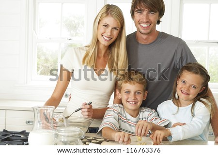 Happy young family in the kitchen with Mum, Dad and their young son and daughter posing together while baking cookies