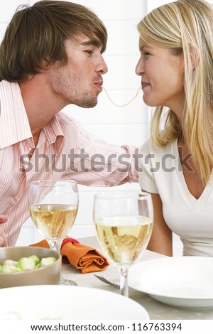 Smiling couple eating spaghetti with the wife eating from one end and the husband the other end of the same strand