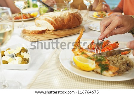 Cropped view image of male hands eating a seafood platter with fried fish and langoustines seated at the dinner table