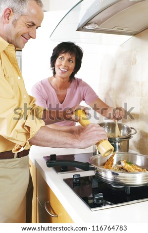 Middle-aged affectionate husband and wife standing at the stove cooking a dinner of fried fish together