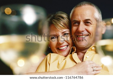 Mature woman embracing his husband between two glasses of white wine - selective focus