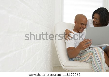 Happy black couple sitting in white armchair with laptop - copy space